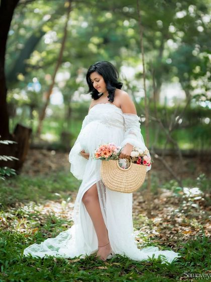 A candid shot of the mother-to-be walking through the woods, holding a basket of flowers. The movement in the gown and the natural setting create a beautiful, dynamic portrait.