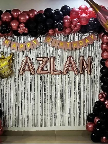 A rose gold and black themed decoration for a 7th birthday at home, featuring a silver fringe curtain and a crown foil balloon.
