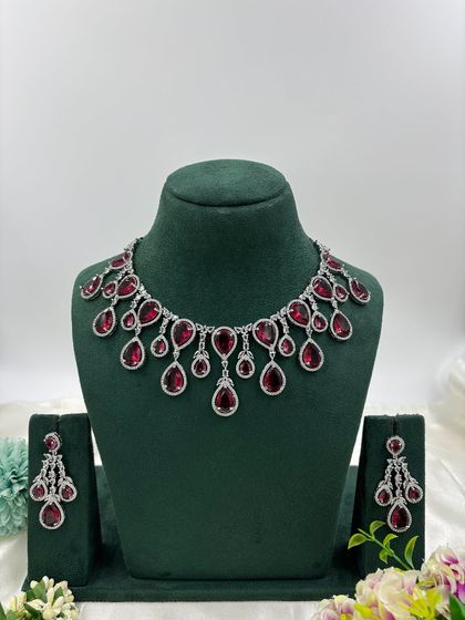 A contemporary silver-plated necklace set with teardrop-shaped stones. This design is available in emerald green, pink, red, and dark blue, offering a sleek and modern look for any occasion.