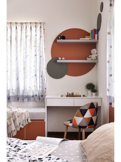 A closer look at the study corner in the kids' room. A simple white desk is set against a creative backdrop of circular painted shapes and floating shelves, creating an inspiring spot for homework and hobbies.