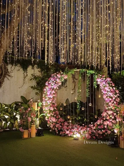 For a modern and romantic engagement, I crafted this stunning circular floral arch. The abundance of pink blossoms, combined with hanging glass orbs and a ceiling of twinkling lights, makes for a perfect photo backdrop and a truly memorable moment.
