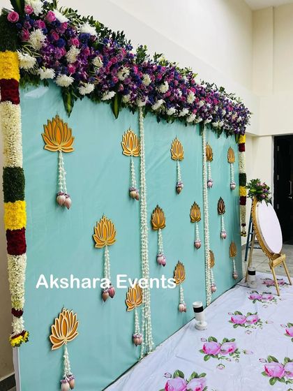 A serene and elegant backdrop for a baby shower. The light blue fabric is adorned with golden lotus cutouts and delicate jasmine flower hangings, creating a peaceful and sophisticated ambiance.