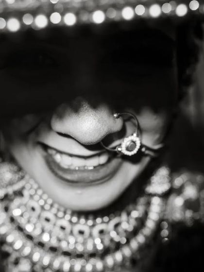 A close-up, artistic shot of a Gujarati bride, her face partially obscured by her veil, highlighting her smile and nose ring.