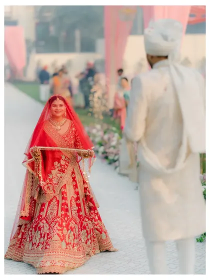The bride's entry, her red lehenga vibrant as she walks towards the groom, a moment of anticipation and love.