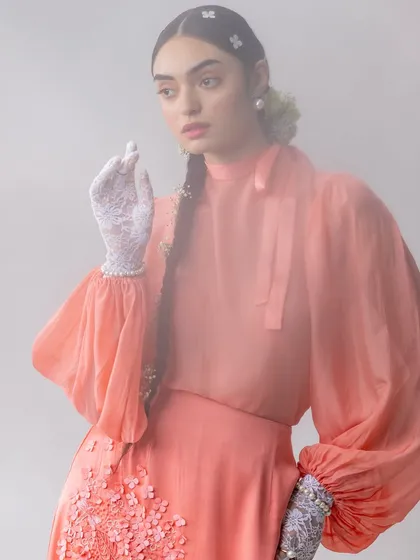 This image captures a moment of soft, ethereal beauty. The styling combines a peach-toned blouse with voluminous sleeves and delicate lace gloves, all enveloped in a soft-focus haze to enhance the dreamy, romantic mood of the shoot.