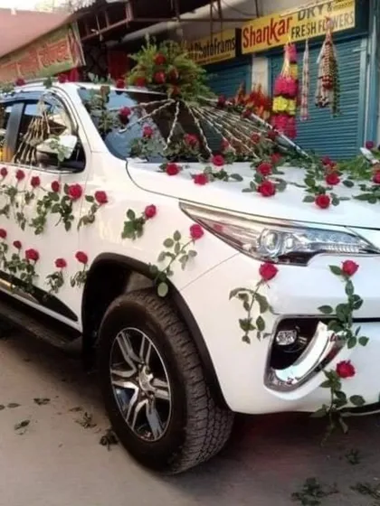 A beautiful wedding car decoration for a white SUV. The design features climbing vines of red roses, creating a romantic and eye-catching look.