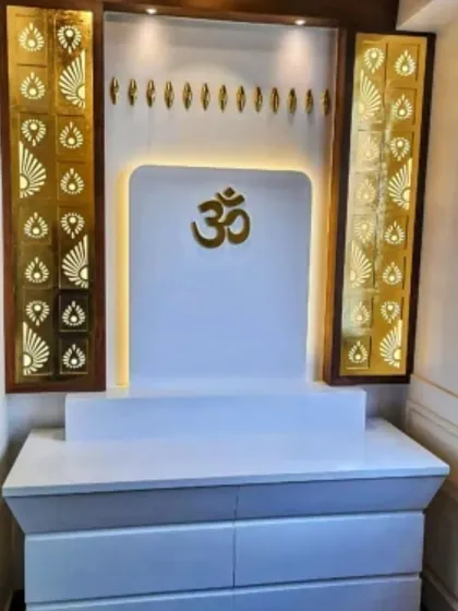 A compact and modern mandir design in white and gold. The back panel features a simple gold "Om" symbol, flanked by two backlit jali panels with a traditional pattern, combining simplicity with a touch of opulence.