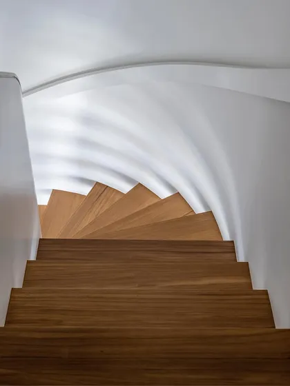 A downward view of the spiral staircase, emphasizing its elegant curve and the beautiful grain of the wood. This feature connects the two floors with architectural grace.