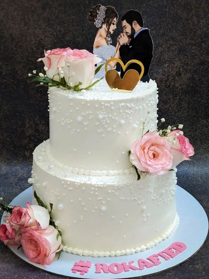 An elegant all-white two-tier cake for a Roka ceremony. This is my popular chocolate mousse cake, decorated with delicate pearls and fresh pink roses for a touch of romance.