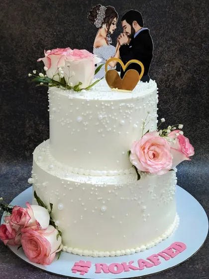 An elegant all-white two-tier cake for a Roka ceremony. This is my popular chocolate mousse cake, decorated with delicate pearls and fresh pink roses for a touch of romance.