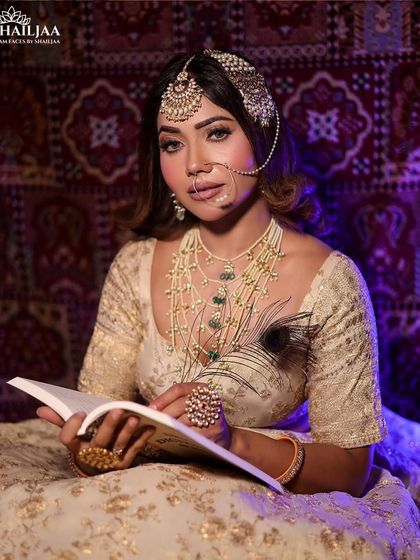 A regal and poised bridal portrait. The makeup features soft, smokey eyes and a contoured base, perfectly complementing the ivory and gold lehenga and creating a look of serene elegance.