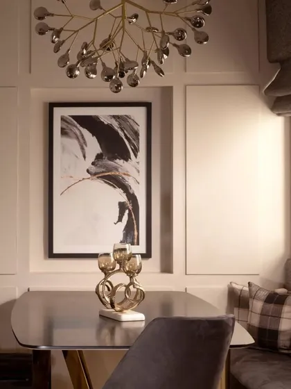 The dining area features a statement chandelier and a large piece of abstract art, framed by classic wall paneling. This combination of modern and traditional elements creates a timeless and elegant dining experience.