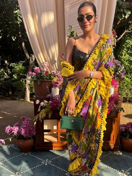 Another look at this vibrant yellow ruffled saree. Paired with a green bag and sleek sunglasses, it’s a perfect example of how to accessorize a modern Indian outfit.