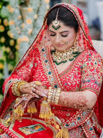 A bride admiring her kalire. Her traditional red lehenga is beautifully accessorized with a kundan and polki set featuring green accents, a classic and timeless choice.