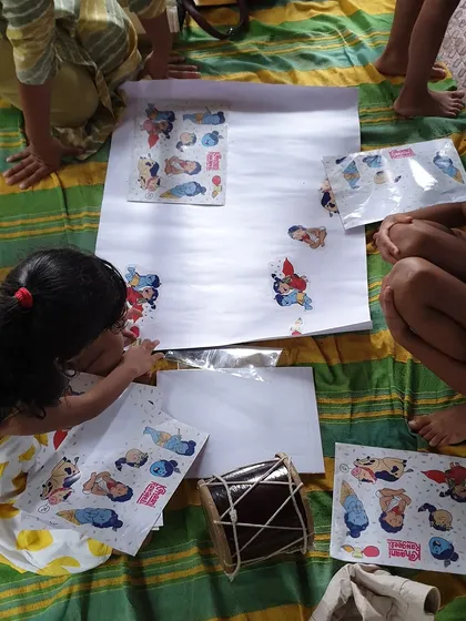 Children gathered around a large sheet of paper, creating a collage with stickers. Collaborative art projects are a wonderful way to build teamwork and friendship.