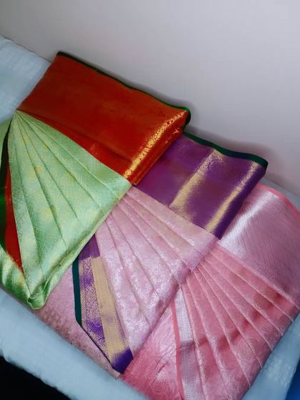 A collection of sarees in pastel shades of green and pink, all pleated and ready for a client. I can handle multiple sarees at once for your convenience.