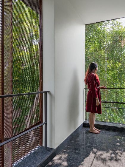A resident enjoys the view from a balcony in the 'Copper House'. The perforated copper screen provides privacy and sun shading while creating a visual connection to the lush greenery outside, demonstrating our focus on functional and beautiful facade design.