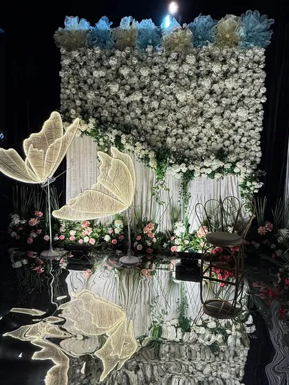 We created this elegant photo booth featuring a dense wall of white flowers and two large, illuminated butterfly props. The reflective flooring doubles the visual impact, making it a magical spot for guests to capture memories.