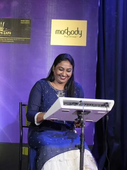 One of our faculty members, Priya Madam, smiling as she plays the rhythm pad, providing musical support for the students' Shiva Bhajan performance.