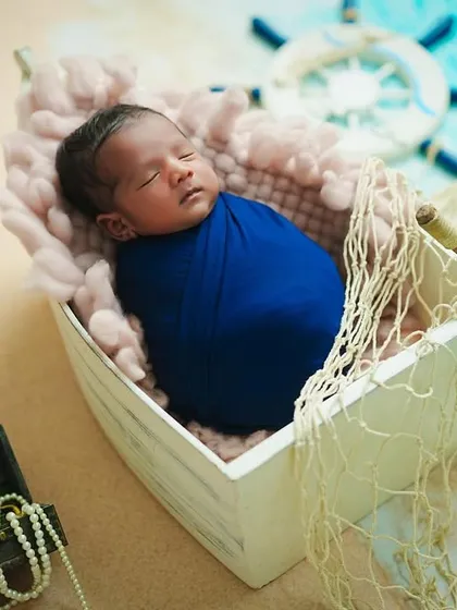 A close-up shot of the newborn sailor, highlighting the textures of the soft blanket and the tiny details of the surrounding props, like the pearl necklace spilling from the treasure chest.