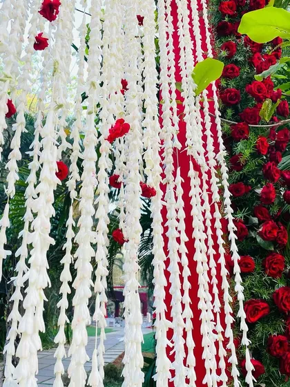 A beautiful close-up of hanging jasmine garlands with pops of red roses, a classic and fragrant detail for any traditional Indian wedding.
