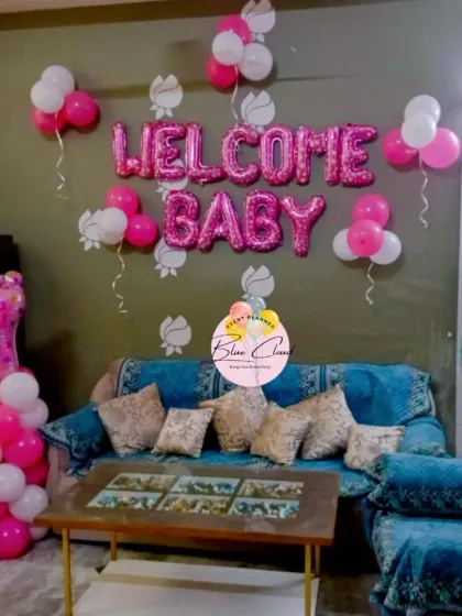 A 'Welcome Baby' girl decoration for a living room, featuring pink and white balloons and a 'It's a Girl' foil balloon pillar.