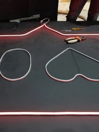 The initial stages of shaping the neon tubes for the 'Heart 0' sign. The glowing red outline begins to take form on the workshop floor.