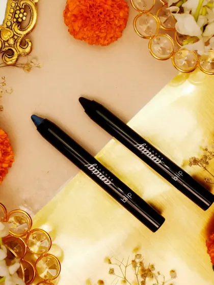A festive flatlay featuring eye pencils surrounded by marigold flowers and decorative gold elements. The warm, vibrant colors are perfect for a Diwali-themed beauty campaign.