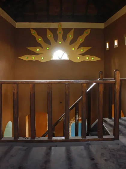 An interior view of a sun mural crafted from mud and recycled glass bottles. This feature, built into the wall of the mud house, not only adds artistic flair but also allows colored light to filter into the space.