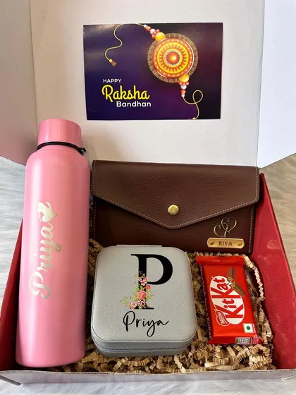 A pretty in pink Rakhi gift set for a sister. This box contains a personalized pink water bottle, a custom jewelry box, and a KitKat, all nestled in a festive gift box.