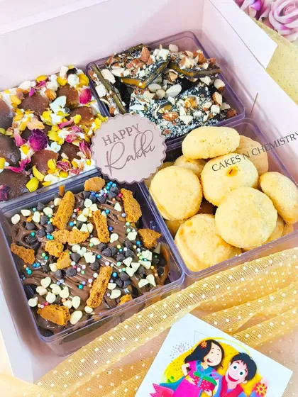 This Rakhi hamper is all about variety. It includes four different treats: chocolate bark with nuts and rose petals, almond brittle, cheese cookies, and a Biscoff chocolate slab.