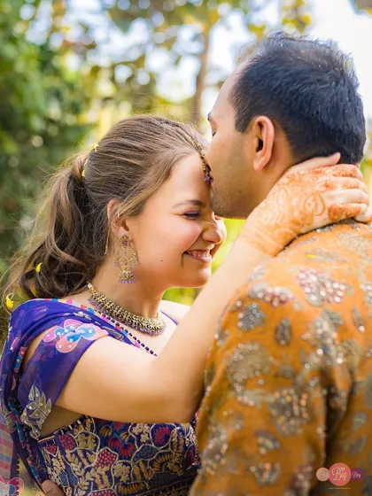 A close-up of a gentle forehead kiss, capturing the bride's joyful smile and the intricate details of her henna.