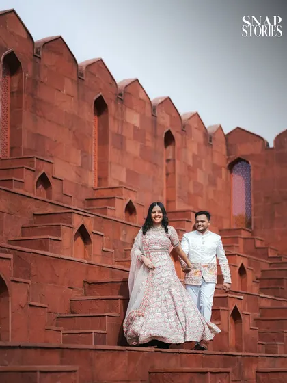 The couple walking hand-in-hand down the steps of a magnificent red sandstone structure, a perfect blend of candid movement and architectural beauty.