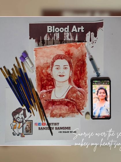 This workstation setup shows a finished blood art portrait next to the reference photo and the tools used. It gives a glimpse into the careful and methodical process behind each piece.