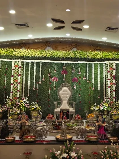 A classic and authentic South Indian stage design featuring a backdrop made entirely of woven green banana leaves (thoranam). The look is completed with hanging tuberose garlands and a regal white throne, ideal for traditional weddings and ceremonies.