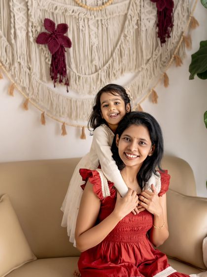 A mother gets a sweet hug from behind by her daughter. The genuine smiles on both their faces make this a truly special and authentic moment.
