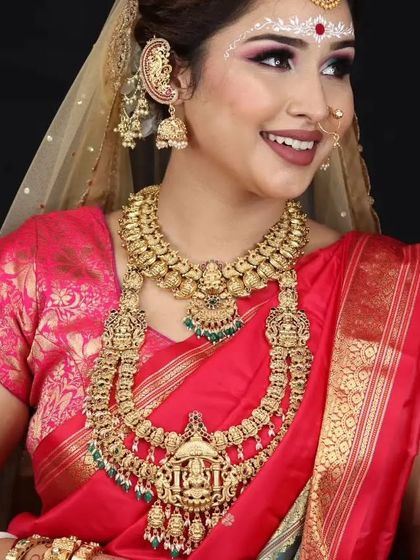 A happy bride combining Bengali and South Indian styles, wearing a heavy temple jewellery set with a traditional Bengali 'kanbala' earring.