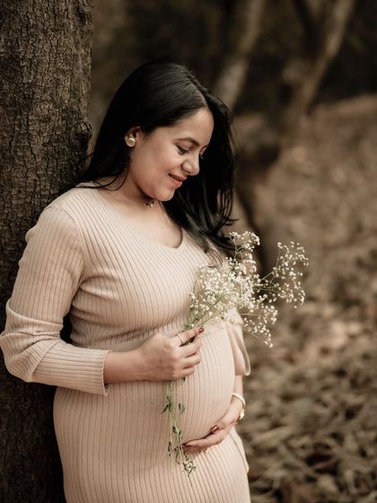 A tender portrait of the mom-to-be leaning against a tree, looking down at the baby's breath she holds against her bump.