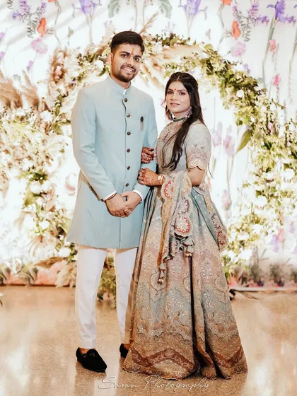A classic full-length portrait of a couple at their Roka ceremony, standing before a beautiful floral arch.