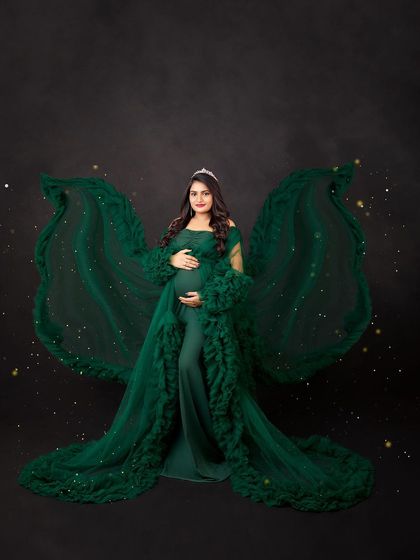 A magical, angelic portrait in a deep green gown with fabric wings, accented by sparkling lights.