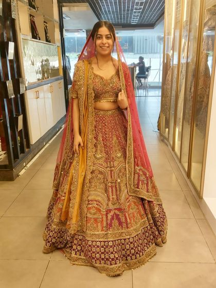 A beautiful bride-to-be trying on a magnificent bridal lehenga with contrasting dupattas in yellow and pink. The intricate embroidery and rich colors make this a standout piece.