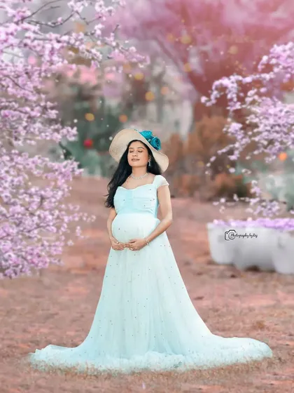 A dreamy solo portrait in a light blue gown and hat, surrounded by edited-in pink blossoms for a fairytale effect.