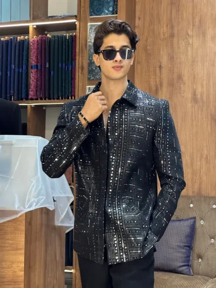 A client posing in a black sequined jacket in our store. The background of fabrics and sewing machines tells the story of our craft.