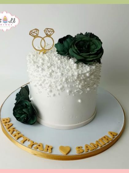 Another view of the elegant pearl-draped engagement cake with deep green roses and a golden ring topper.