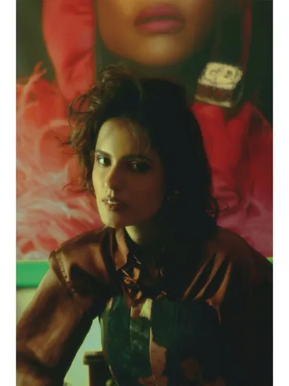A close-up on the model's face, set against a bold, red background. The focus is on her expression of newfound strength, with the styling serving as her armor.