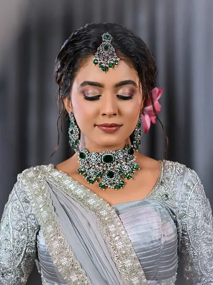 A close-up of a soft glam look with a grey saree and emerald jewelry, showing the eyes closed to highlight the eyeshadow blend.