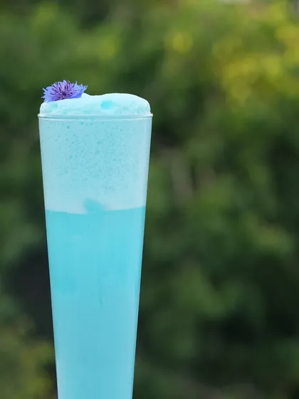 A close-up of the Blue Velvet cocktail against a natural green backdrop. It's the perfect photogenic drink for a daytime event on the terrace.