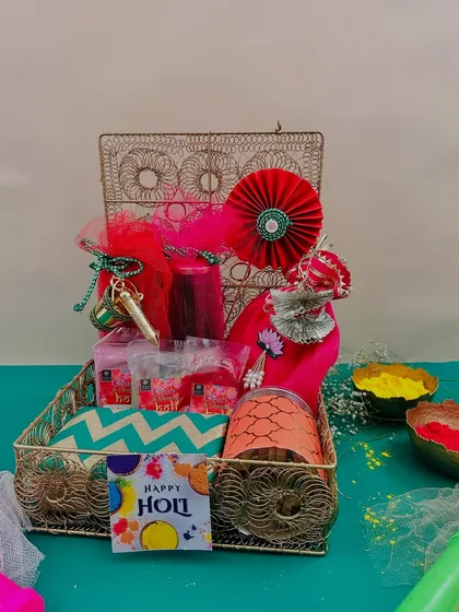 A festive red and gold Holi hamper in a wire box. The combination of a chevron pouch, colorful potlis, and gulal packets makes it a complete and vibrant gift.