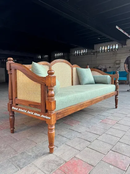 A colonial-style daybed with turned legs and a caned back, finished in a rich teak polish.