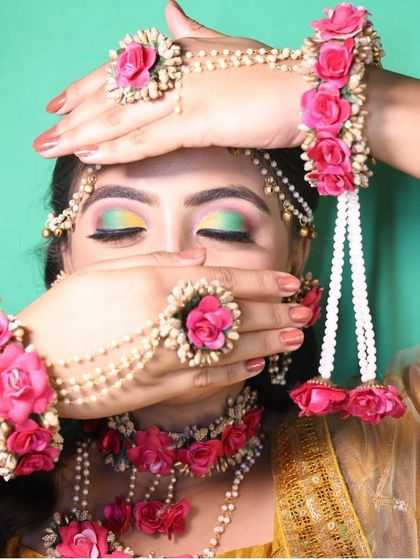 A playful shot showing the full floral necklace and hath phool. The colorful eye makeup perfectly complements the vibrant pink of the floral jewellery.